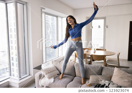Energetic woman dancing, singing and jumping barefoot on cozy sofa 123923074