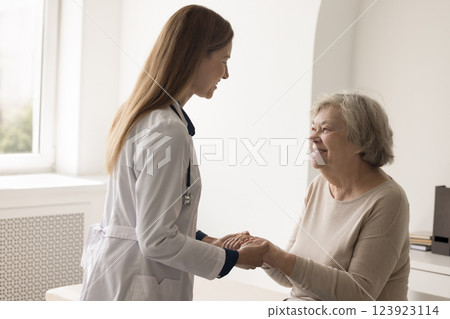 Compassionate young female doctor holding hands of elderly patient grandma 123923114