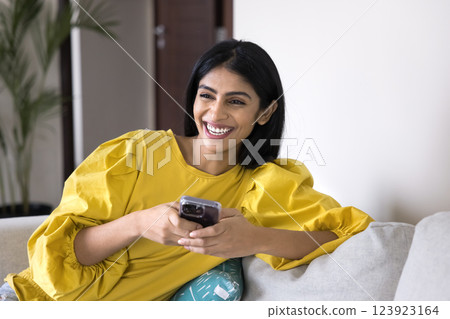 Happy Indian woman relaxing on sofa at home with smartphone Happy Indian woman relaxing on sofa at home with smartphone 123923164