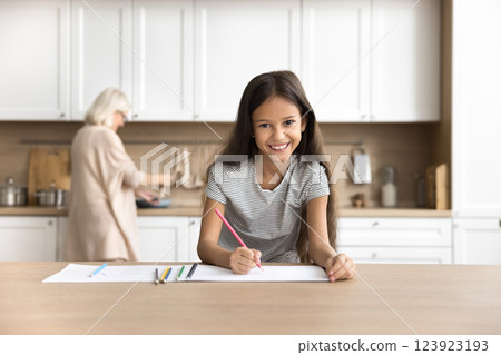 Smiling tween girl drawing while aged grandma cooking at kitchen 123923193