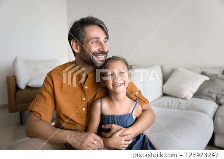 Calm man cuddling little daughter seated together on comfortable sofa Calm man cuddling little daughter seated together on comfortable sofa 123923242
