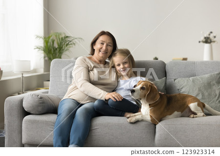 Kid sits on sofa with grandmother and cute beagle puppy Kid sits on sofa with grandmother and cute beagle puppy 123923314