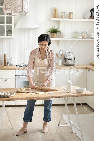 Confident mature woman flattening dough with rolling pin in kitchen 123923346