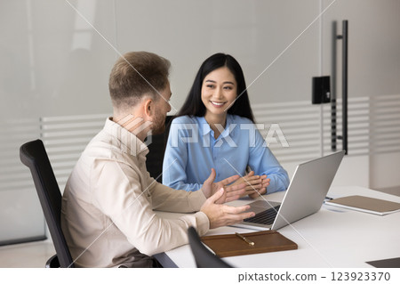 Confident young businessman consulting young Asian female using notebook Confident young businessman consulting young Asian female using notebook 123923370