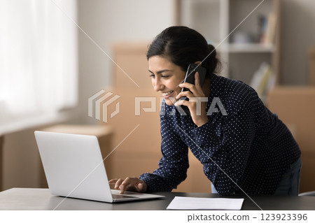 Smiling young female sales manager speak on phone using notebook 123923396