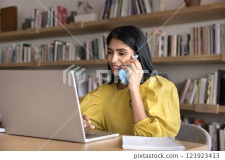 Young woman engaged in work on notebook hold phone conversation 123923413