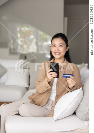 Positive satisfied young Asian consumer shopping on mobile phone Positive satisfied young Asian consumer shopping on mobile phone 123923423