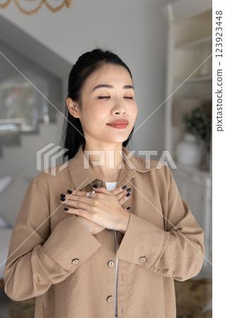 Positive peaceful young adult Asian girl feeling own heartbeat 123923448