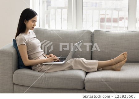 Asian woman working, studying on laptop settled down on sofa Asian woman working, studying on laptop settled down on sofa 123923503