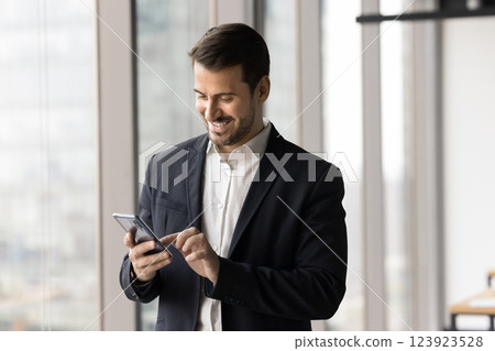 Smiling businessman dressed in suit using modern smartphone in office 123923528