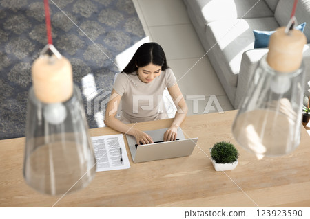 Woman typing on laptop seated at wooden table, overhead view 123923590