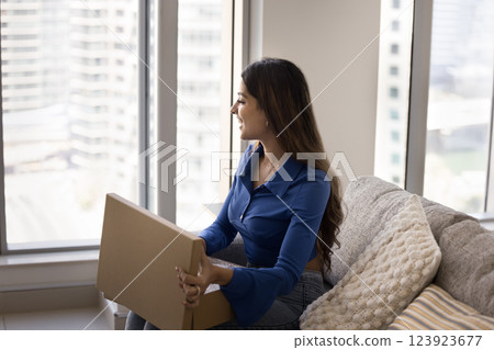 Pensive smiling woman sit on sofa with parcel on laps Pensive smiling woman sit on sofa with parcel on laps 123923677