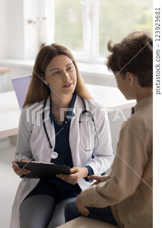 Friendly young woman pediatrician interviewing little boy at clinic office Friendly young woman pediatrician interviewing little boy at clinic office 123923681