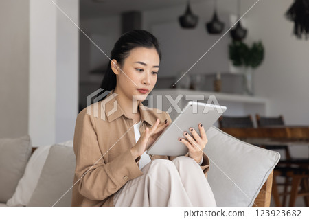 Focused young Asian woman using digital online technology on tablet 123923682