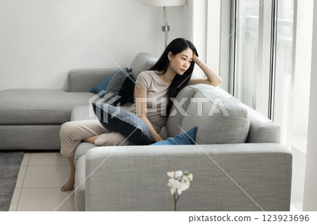 Pensive sad Asian woman sitting on sofa in living room 123923696