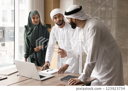 Three Muslim professionals engaged in discussion around laptop in office Three Muslim professionals engaged in discussion around laptop in office 123923734