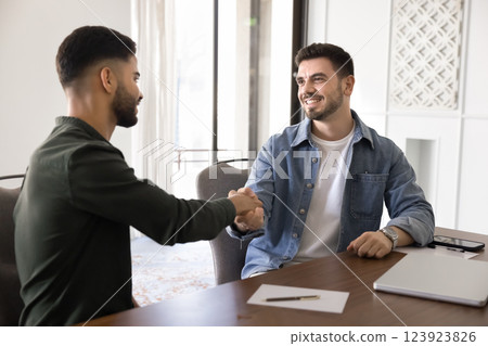 Two smiling Arabian businessman shaking hands seated at desk 123923826
