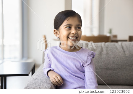 Cute Indian girl looking into distance seated on couch 123923902