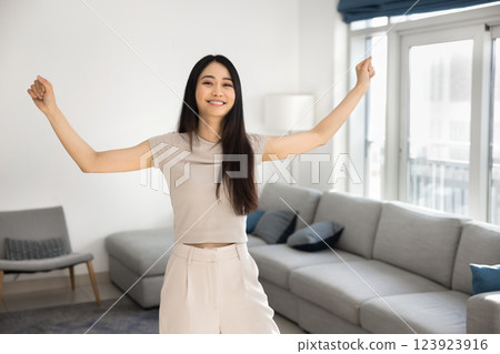 Young joyful Asian woman stands in modern, well-furnished living room 123923916