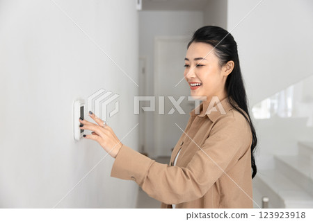 Happy young Asian homeowner woman typing on climate control panel, 123923918