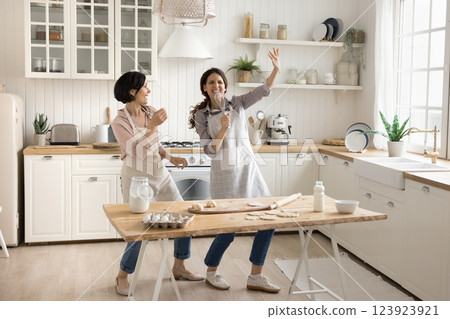 Overjoyed young woman sing songs at kitchen with senior mother 123923921