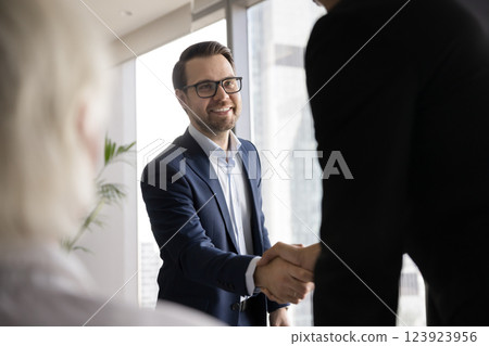 Smiling young businessman handshake with partner on stakeholders group meeting Smiling young businessman handshake with partner on stakeholders group meeting 123923956