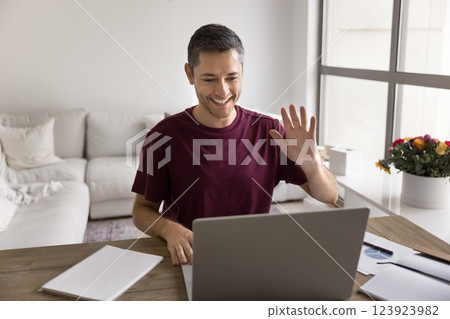 Young man greeting videocall participant sitting at table at home Young man greeting videocall participant sitting at table at home 123923982