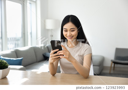 Pretty Asian woman sitting at table holding her phone Pretty Asian woman sitting at table holding her phone 123923993