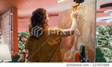 In a rustic workshop, artist mixes a variety of watercolor paint on palette to create a colorful masterpiece on canvas. Woman painting with a brush and showing her skill, artwork creation. Camera A. In a rustic workshop, artist mixes a variety of watercolor paint on palette to create a colorful masterpiece on canvas. Woman painting with a brush and showing her skill, artwork creation. Camera A. 123923996