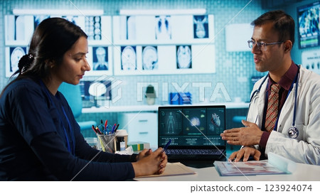 Indian expert explaining diagnostics through test results with a female patient at medical office, doing scan interpretation at check up with woman. Healthcare services on insurance. Camera B. 123924074