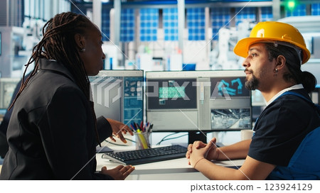 Photovoltaics factory worker discussing with woman about system performance. Solar panels manufacturing plant african american manager chatting with engineer about energy production, camera A 123924129