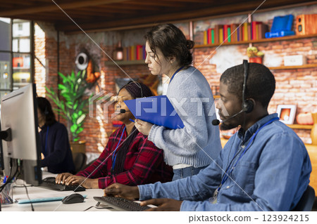 Call center team leader supervising agents at office desk handling customer inquiries, complaints and support requests. Customer service manager overseeing workers assisting clients 123924215