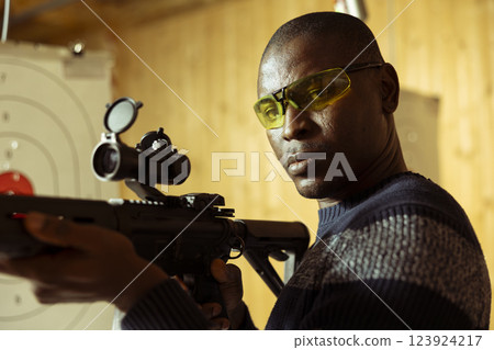 Portrait of man in indoor shooting range offering rental semiautomatic weapons for tryouts, doing training. Novice in firing range getting hands on experience with rifle, sharpening skills, close up Portrait of man in indoor shooting range offering rental semiautomatic weapons for tryouts, doing training. Novice in firing range getting hands on experience with rifle, sharpening skills, close up 123924217