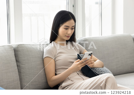 Serious Asian woman sitting on sofa hold smartphone 123924218