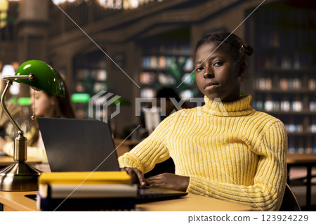 Schoolgirl reading information via internet and taking notes in a library, focusing on theoretical studies and completing her class assignments in an academic environment. Educational work. 123924229