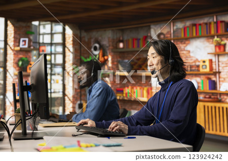 Team of customer service staff members tracking support ticket in dedicated company software on PC. Asian call center worker and african american colleague talking with customer calling 123924242