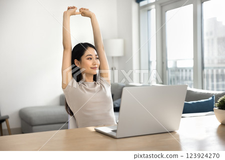 Woman take break, stretching arms seated at desk with laptop Woman take break, stretching arms seated at desk with laptop 123924270