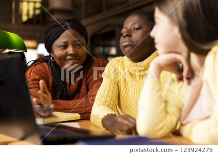 Preteen scholars collaborating with their tutor in a learning environment, working on school projects and developing critical classroom skills. Woman mentoring her students in the library. Preteen scholars collaborating with their tutor in a learning environment, working on school projects and developing critical classroom skills. Woman mentoring her students in the library. 123924276