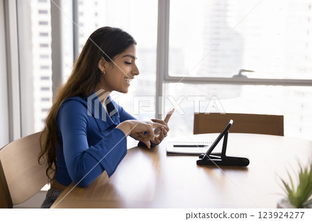 Young 20s Indian woman sitting at table, engaged in videocall Young 20s Indian woman sitting at table, engaged in videocall 123924277