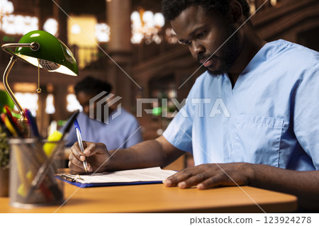 African american medical student creates a summary of class notes to learn easily for an exam, collecting information from the library to complete his knowledge. Future doctor at desk. African american medical student creates a summary of class notes to learn easily for an exam, collecting information from the library to complete his knowledge. Future doctor at desk. 123924278