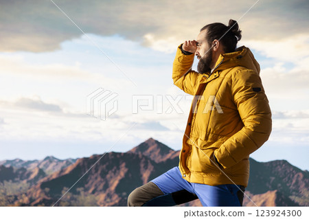Male hiker looks out over a breathtaking mountain range from the hill top, embracing the solitude and fresh air of the great outdoors. Sense of adventure and endless nature exploration. 123924300