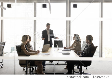Stakeholders sit at conference table listening speech of businessman standing Stakeholders sit at conference table listening speech of businessman standing 123924326
