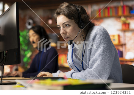 Call center employee using headset microphone to answer customers technical inquiries, assisting with questions about hardware issue. Woman doing customer service job using PC to troubleshoot problems 123924331