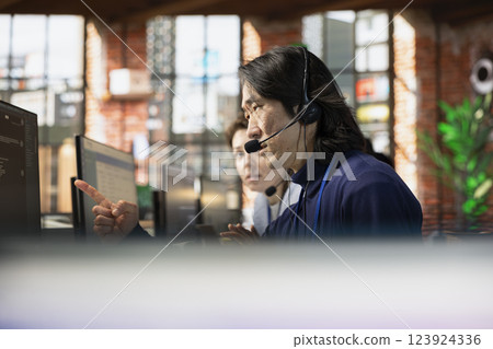 Senior call center agent using headphones microphone to answer customers technical inquiries about hardware issue. Experienced Asian worker doing customer support job using PC to troubleshoot problems Senior call center agent using headphones microphone to answer customers technical inquiries about hardware issue. Experienced Asian worker doing customer support job using PC to troubleshoot problems 123924336