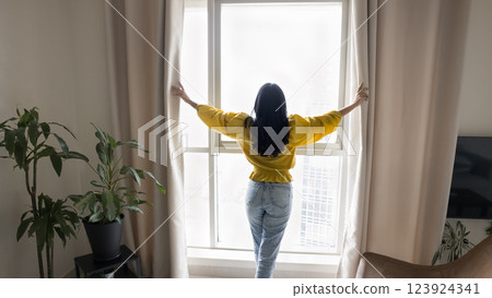 Rearview woman standing in front of window and opening curtains 123924341