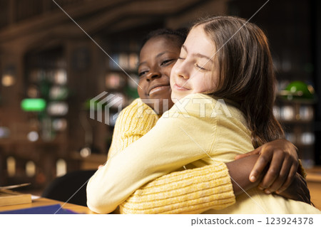 Sweet teenage girls having fun laughing and gossiping together in a public library, joking around and feeling happy with their friendship. Diverse scholars enjoying a discussion after classes. Sweet teenage girls having fun laughing and gossiping together in a public library, joking around and feeling happy with their friendship. Diverse scholars enjoying a discussion after classes. 123924378