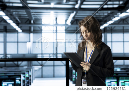 System administrator in data center uses automation tools on tablet, running predictive maintenance routines. IT expert ensuring continuous uptime of server farm, managing data flows with device 123924381