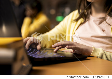 School pupil competing her class notes on her laptop during a homework session, working on exercises in the public library. Teenager focusing on modern ways to finish assignments. Close up. 123924391