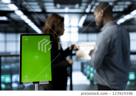 Green screen mockup tablet in front of technicians in blurry background working in server farm, analyzing data. Close up of chroma key tablet next to workers supervising data center 123924396