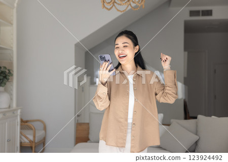 Happy adult Asian girl holding mobile phone and dancing 123924492